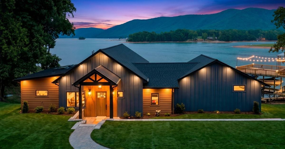 Exterior of a well-lit custom home by Grace Alon Builders at dusk with Smith Mountain Lake, mountains, and a sunset sky in the background.