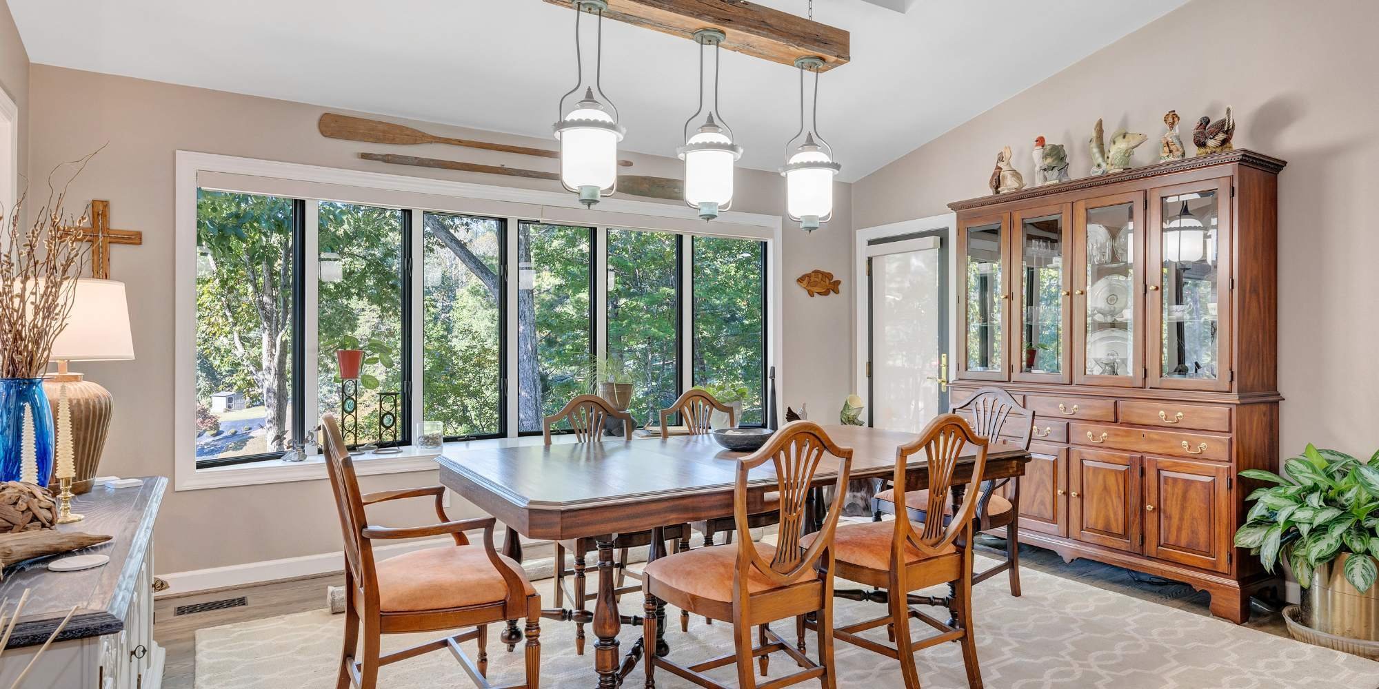 Home addition featuring a sunlit dining room with glass hutch, wood table, and nature views Smith Mountain Lake