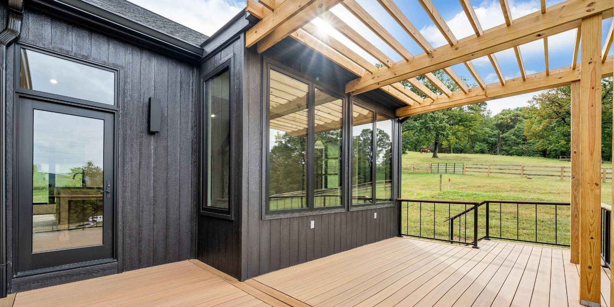 Exterior view of a home addition in Roanoke, VA with black siding and an attached deck with a pergola by Grace Alon Builders