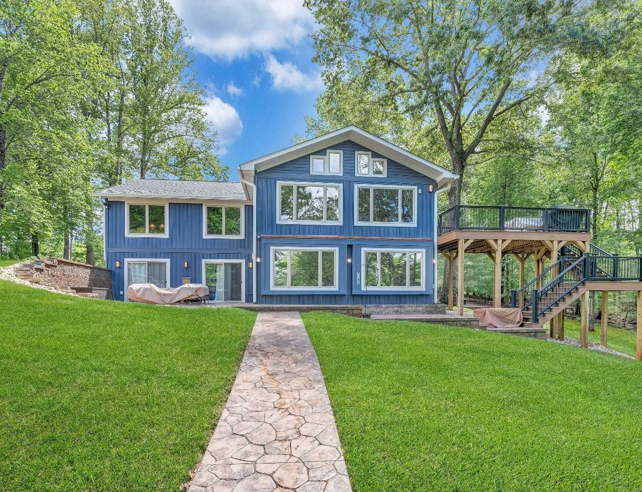 Exterior of a lakefront custom home with blue siding, large windows, and a multilevel deck by grace Alon Builders in Goodview, VA